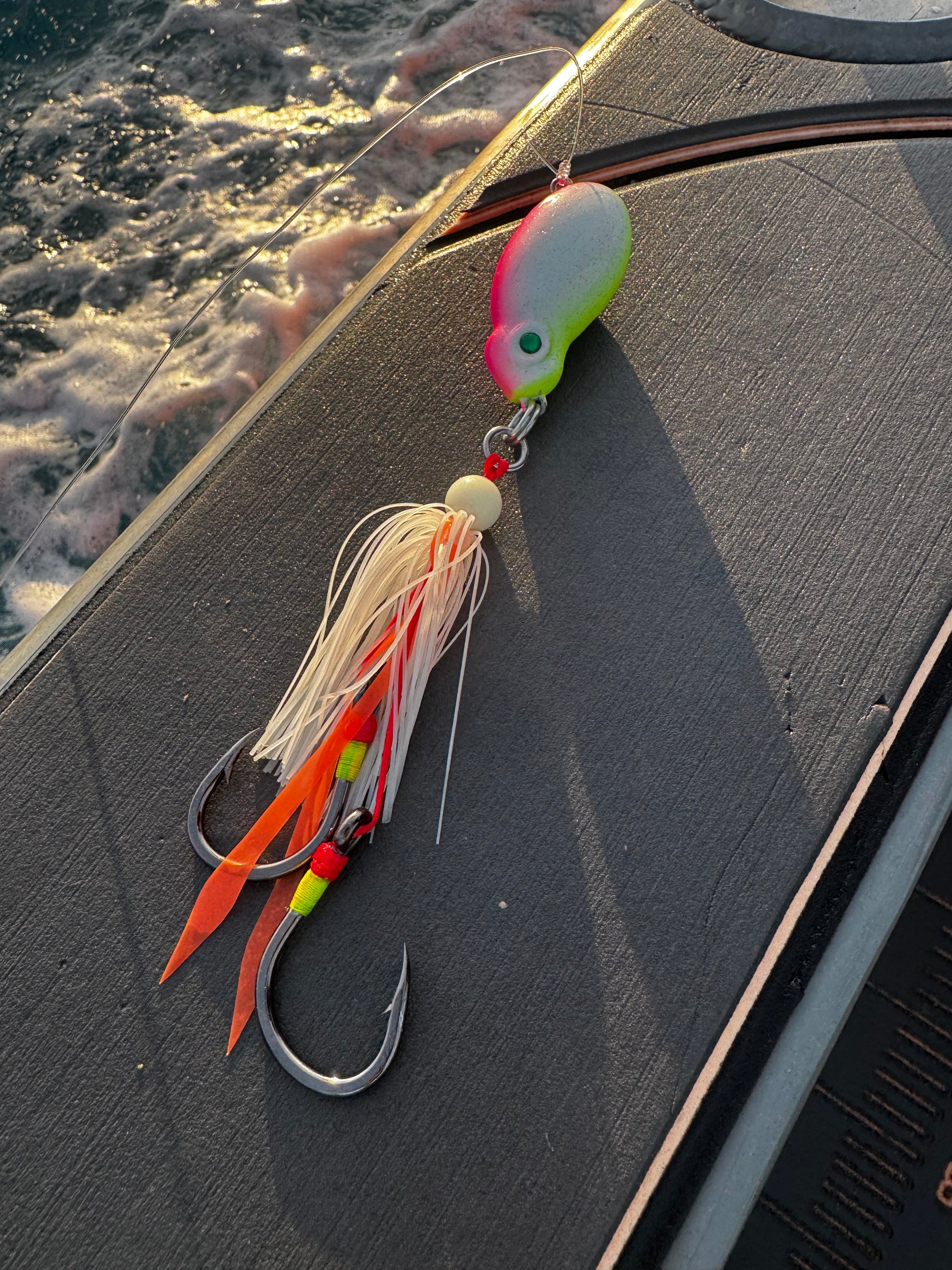 Frothy Okky jig in pink and glow with orange flash ribbons on the boat gunwale